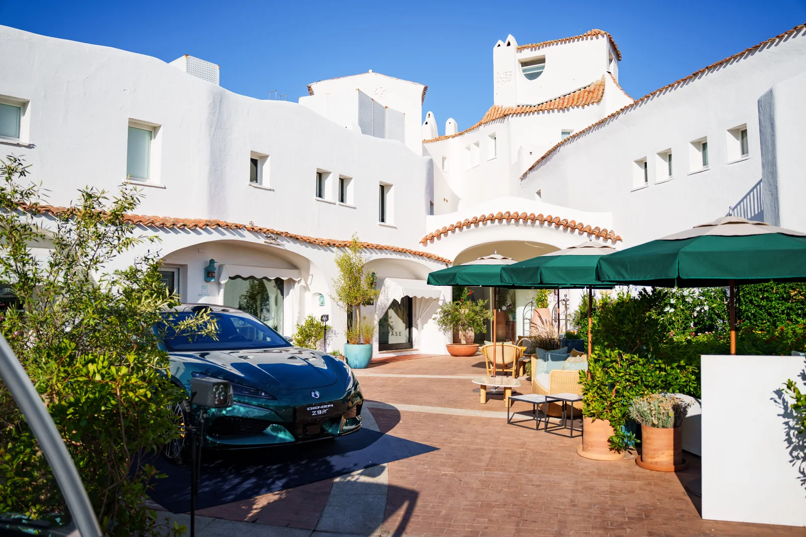 A green Denza Z9 GT parked in the whitewashed courtyard of Romazzino, A Belmond Hotel in Porto Cervo