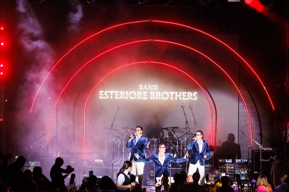 The Esteriore Brothers perform in blue velvet jackets on a stage lit by red neon arches
